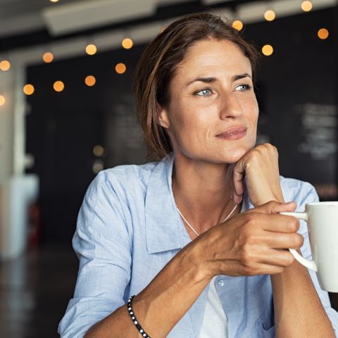 Thoughtful,Mature,Woman,Sitting,In,Cafeteria,Holding,Coffee,Mug,While